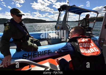 Coast Guard Petty Officer 2nd class Paul Quaife, eine Maritime Durchsetzung Spezialist in Seattle stationiert mit dem Sektor Puget Sound Boarding Team, Chats mit einem Stellvertreter aus der Kootenai County Sheriff Office am Lake Coeur d'Alene, Idaho, 1. Juli 2018. Die Küstenwache Boot Besatzungen das Wasser patrouillierten und arbeitete lokale Seemänner, wie Schiff sicher zu erziehen. Stockfoto