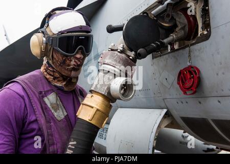 Philippinischen MEER (Juli 04, 2018) der Luftfahrt Bootsmann Mate (Kraftstoff) Airman Drexler Davis Kraftstoffe ein Flugzeug auf dem Flugdeck der Flugzeugträger USS Ronald Reagan (CVN 76). Ronald Reagan ist das Flaggschiff der Carrier Strike Group 5, die eine Bekämpfung bereit, Kraft, schützt und verteidigt die kollektive maritime Interessen seiner Verbündeten und Partnern in der indopazifischen Region. Stockfoto