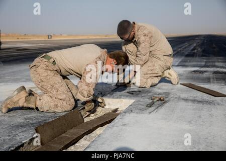 Unbekannten ORT, NAHER OSTEN - US Marine Corps Cpl. Evelyn Jones (links), einen Admin und Operations Specialist und Cpl. James Fixin (rechts), ein Wartungstechniker mit Marine Wing Support Squadron 371 bereiten Sie ein Abschnitt der Fahrbahn während der Reparatur eines beschädigten Flugplatz Juli 3, 2018. Der Flugplatz Schäden reparieren Team sorgt für Start- und Landebahnen sicher sind Flugbetrieb in der gesamten Region durchzuführen. Stockfoto