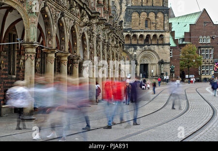 Bremen, Deutschland - Verschwommenes menschliche Figuren die Straße und Straßenbahnschienen überqueren vor dem historischen Rathaus und der Kathedrale (lange Belichtung) Stockfoto