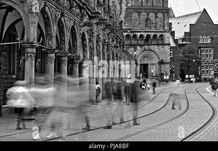 Bremen, Deutschland - Verschwommenes menschliche Figuren die Straße und Straßenbahnschienen überqueren vor dem historischen Rathaus und der Kathedrale (lange Belichtung, monochrom Stockfoto