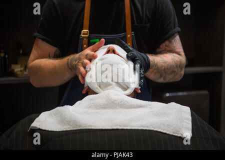Berlin, Deutschland. 05 Sep, 2018. 05.09.2018, Berlin: ein Friseur legt warme Handtücher über das Gesicht eines Mannes. Credit: Arne Immanuel Bänsch/dpa/Alamy leben Nachrichten Stockfoto