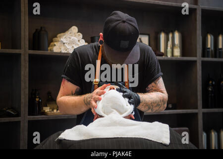 Berlin, Deutschland. 05 Sep, 2018. 05.09.2018, Berlin: ein Friseur legt warme Handtücher über das Gesicht eines Mannes. Credit: Arne Immanuel Bänsch/dpa/Alamy leben Nachrichten Stockfoto