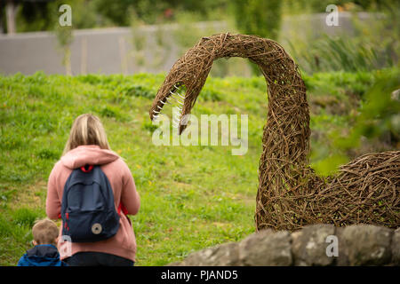 Willow gewebter Jurassic Dinosaur mit Besuchern im RHS Garden, Harlow Carr, Harrogate, North Yorkshire, England, VEREINIGTES KÖNIGREICH. Stockfoto