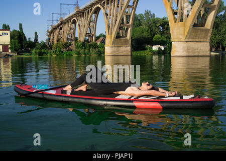 Schöne Mädchen liegt am Stand up Paddle Board, Yoga von schönen Mädchen auf der helle Stadt Hintergrund durchgeführt Stockfoto