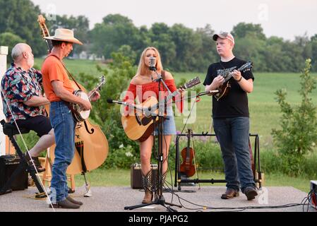 Bluegrass Music Performer spielen live Musik mit Banjo, Gitarren, Geige, ausserhalb des Konzert in der Landschaft bei Sonnenuntergang, außerhalb Monroe, Wisconsin, USA Stockfoto