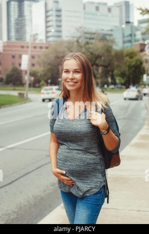 Glückliche gesunde Schwangerschaft. Portrait der kaukasischen schwangere junge blonde kaukasische Frau wandern in belebten Stadt außerhalb. Schöne schlanke sportliche erwarten Stockfoto