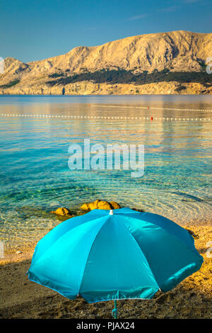 Ein einsamer Sonnenschirm am Strand bei Tagesanbruch am Wasser der Adria in Baska auf der Insel Krk Stockfoto