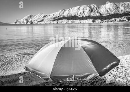 Ein einsamer Sonnenschirm am Strand bei Tagesanbruch am Wasser der Adria in Baska auf der Insel Krk Stockfoto