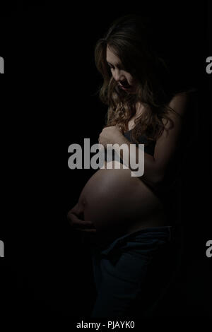 Eine schwangere asiatische Frau zur Seite stellen, nach unten schaut. Eine dunkle künstlerische Portrait. Stockfoto