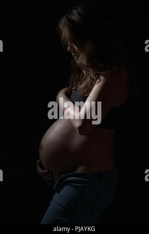 Eine schwangere asiatische Frau zur Seite stellen, nach unten schaut. Eine dunkle künstlerische Portrait. Stockfoto