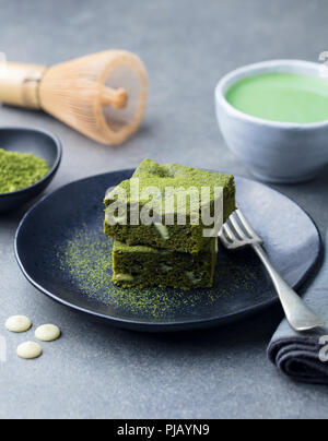 Matcha grüner Tee Kuchen, Bars, Brownie mit weißer Schokolade auf einem Teller. Grauen Stein Hintergrund. Stockfoto