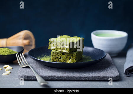 Matcha grüner Tee Kuchen, Bars, Brownie mit weißer Schokolade auf einem Teller. Grauer Hintergrund. Kopieren Sie Platz. Stockfoto