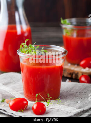 Tomatensaft im Glas mit kresse Salat, frische Tomaten auf Holz Schneidebrett und grau Handtuch. Stockfoto