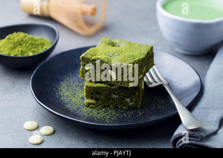 Matcha grüner Tee Kuchen, Bars, Brownie mit weißer Schokolade auf einem Teller. Grauer Hintergrund. Stockfoto