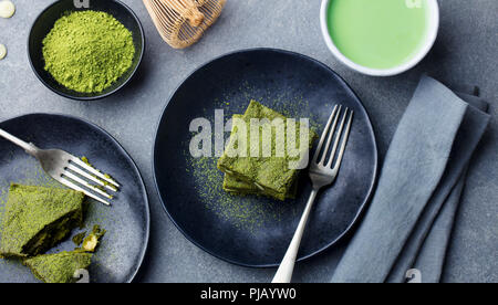 Matcha grüner Tee Kuchen, Bars, Brownie mit weißer Schokolade auf einem Teller. Grauer Hintergrund. Ansicht von oben. Stockfoto