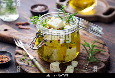 Feta Käse, mariniert in Olivenöl mit frischen Kräutern in Glas. Holz- Hintergrund. Stockfoto