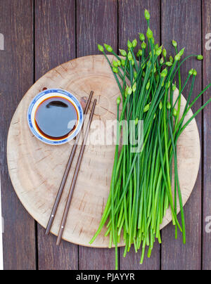 Schnittlauch Blüte, Knoblauch, Schnittlauch oder Allium tuberosum auf einem Schneidebrett. Holz- Hintergrund. Ansicht von oben. Stockfoto