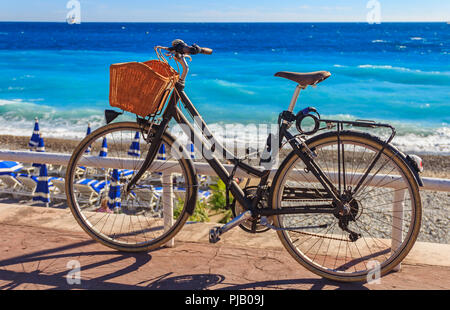 Fahrrad mit einem Weidenkorb auf der berühmten Promenade des Anglais mit dem Mittelmeer im Hintergrund in Nizza, Frankreich. Stockfoto