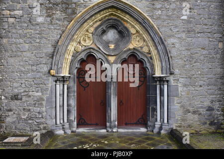 Gewölbte double Gate mit Holztüren auf Metall Scharniere an der Seitenwand der mittelalterlichen Kirche aus Stein. Stockfoto