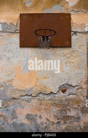 Sie suchen ein altes rostiges Metall Basketballkorb mit Netz einer alten Mauer, dass Risse hat geschraubt, abblätternde Farbe und fehlende Mauerwerk Stockfoto