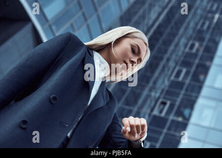 Frau mit Blick auf ihr Handgelenk beobachten, während die Kontrolle der Zeit gehen auf die Stadt Hintergrund Stockfoto
