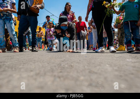 Eine mexikanische Verehrer von Santa Muerte (Heilige Tod), sein baby boy Holding, kriecht auf seinen Knien während einer religiösen Wallfahrt in Mexiko City, Mexiko. Stockfoto