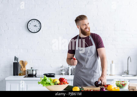 Schöner Lächeln bärtigen Mann in Schürze Musik im Kopfhörer und weg schauen, beim Kochen in der Küche Stockfoto