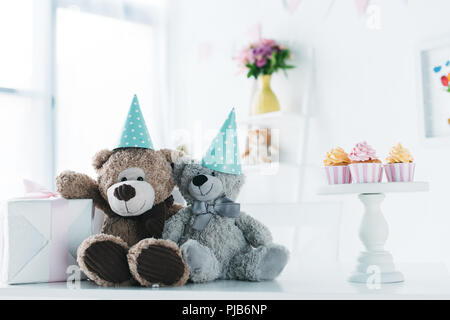 Teddybären in Kegel auf Tabelle mit Geschenkbox und Muffins Stockfoto