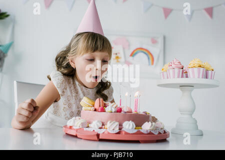 Adorable Zicklein in der Kegel Kerzen ausblasen von Geburtstag Kuchen auf dem Tisch Stockfoto