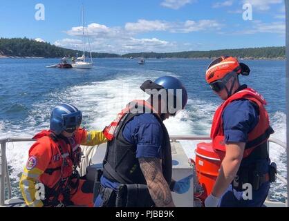 Eine Aviation überleben Techniker, von Air Station Port Angeles und Unteroffiziere 3. Klasse Jordanien Harlacher und Matthew Boyd, beide 45-Fuß-Antwort Boat-Medium boot Crewmitglieder von Station Bellingham neigen dazu, eine verletzte Frau in der Nähe von sucia Island, Washington, 2. Juli 2018. Die 70-jährige Frau wurde verletzt, als das Segelschiff, im Hintergrund lief in der Nähe von sucia Island lief. Us-Küstenwache Stockfoto