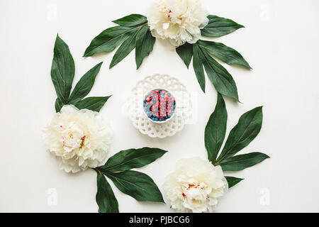 Eine Tasse mit verschiedenen Beeren gefüllt steht auf grünen Blättern. Konzept der gesunden Ernährung oder Diät. Stockfoto