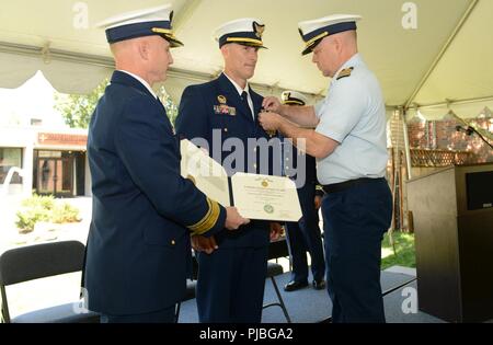 Chief Warrant Officer Christopher Chef, kommandierender Offizier Coast Guard Cutter Bluebell, ist mit der Coast Guard Commendation Medal von Hinten Adm vorgestellt. David Throop, der Kommandant der Küstenwache 13. Bezirk, und Kapitän Thomas Griffitts, kommandierender Offizier Marine Safety Unit Portland, die während eines Befehls Zeremonie für den Cutter Bluebell an der MSU Portland, 12. Juli 2018 statt. Boss wurde für seine Verdienste während seiner Amtszeit als kommandierender Offizier der Pazifischen Nordwesten ältesten operativen Coast Guard Cutter einschließlich einer 10-monatigen Drydock wo das Werkzeug hatte repowered zu sein. U.S Stockfoto