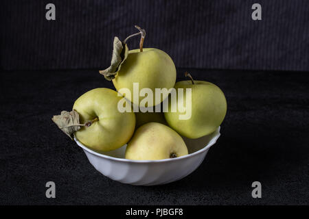 Vier frische grüne Äpfel in Weiß Schüssel auf schwarzem Hintergrund Stockfoto