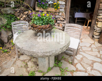 Steintisch mit Blumen und Stühle im Garten, Steinboden Stockfoto