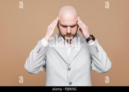 Kopfschmerzen und Schmerzen. Portrait von mittleren Alters kahlen bärtigen Geschäftsmann in hellen grauen Anzug mit schmerzhaften Kopf. indoor Studio shot, isoliert auf lig Stockfoto