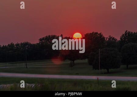 Orange Ball der untergehenden Sonne in der Oklahoma, USA Landschaft. Glühende, rosa und lila Himmel. Stockfoto