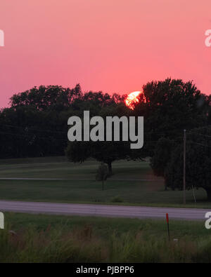 Orange Ball der untergehenden Sonne in der Oklahoma, USA Landschaft. Glühende, rosa und lila Himmel. Stockfoto