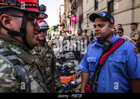 Armee finden Spc. Jason Delgado, 328 unterstützen Hosptial, spricht mit einem Sanitäter mit der New Yorker Feuerwehr, bevor Sie eine simulierte chemischen Angriff in Manhattan, New York, Juli, 10, 2018. Diese Soldaten sind Teil eines National Response Element, das mit der zivilen Behörden manpower, Fahrzeuge und Ausrüstung zu bieten medizinische Leistungen zu erbringen sowie chemische, biologische und radiologische clean up - Fähigkeiten, die in der hohen Nachfrage im Falle einer Katastrophe oder angreifen würde. Stockfoto