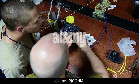 Senior Airman Julian Hamner, 407 Expeditionary Communications Squadron Kabel und Antenne Techniker, Uhren als Oberst Scott Gibson, 407 Air Expeditionary Gruppenkommandant, setzt einen Abisolierte LWL in eine Maschine, Juli 18, 2018, an einem geheimen Ort im Südwesten Asien. Die 407 ECS zur Verfügung gestellte Führung mit einem Hands-on Look in die täglichen Operationen der Squadron verbessern ihr Verständnis von Mission die Fähigkeiten des Geräts. Stockfoto