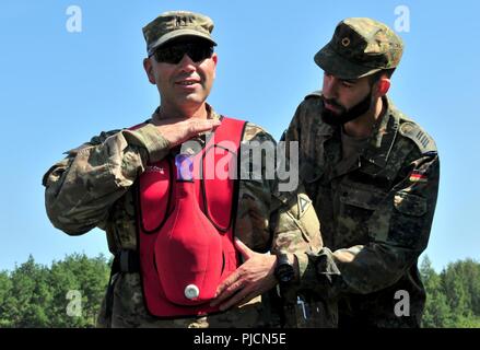 Die US-Armee Beobachter/coach Trainer der Joint Multinational Readiness Center Falcon's Team zugewiesen, hilft bei der Deutschen Bundeswehr Reservisten mit Erste-hilfe-Verfahren Vor medizinische Luft evakuierungsübung an JMRC von Hohenfels, Hohenfels, Deutschland, 19. Juli 2018. Ein Gerät, das hilft, das Heimlich Manöver Praxis verschlissen ist, dass die Teilnehmer Hilfe in wie stark er Brust des Opfers zu komprimieren. Nebraska und Kansas Army National Guard Soldaten beteiligen sich an multinationalen Interoperabilität Ausbildung, mit der die Beziehung zwischen den USA und der Ho verbessert Stockfoto