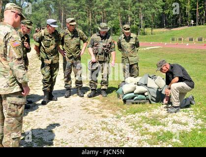 Eine zivile Beobachter/coach Trainer der Joint Multinational Readiness Center zugeordnet, hilft bei der Deutschen Bundeswehr Reservisten mit Improvised Explosive Device Anerkennung auf Hohenfels training Bereich der Gemeinsamen Multinationalen die Bereitschaft, Hohenfels, Deutschland, Juli 19, 2018 Zug. Nebraska und Kansas Army National Guard Soldaten beteiligen sich an multinationalen Interoperabilität Ausbildung, mit der die Beziehung zwischen den USA und dem Gastgeberland verbessert. Stockfoto