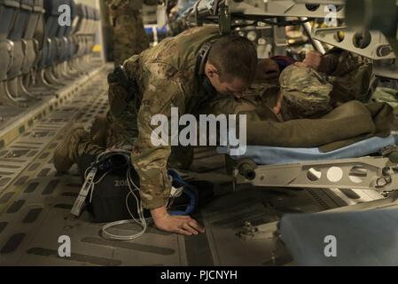 Senior Airman Kyle Caldwell, Flug Medic, 455Th Expeditionary Aeromedical Evacuation Squadron (Eaes), Flughafen Bagram, Afghanistan, kommuniziert mit seinen Patienten über die Summen der C-17 Globlemaster III Jet Engines während der periodischen Prüfung auf dem Weg zur Air Base Ramstein, Deutschland, 21. Juli 2018. Die Flieger der 455th EAES sind damit beauftragt, mit dem Transport von USA und NATO-Partner Service Mitglieder zur Langzeitpflege Behandlungsanlagen verletzt. Stockfoto