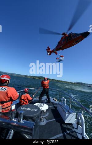 Besatzungsmitglieder an Bord der 52-Fuß-Motor Life Boat Intrepid von der Coast Guard Station Coos Bay Verhalten rescue Warenkorb hoist Training mit einem MH-65 Dolphin Hubschrauberbesatzung aus Sektor North Bend, Erz, 19. Juli 2018. Die Küstenwache führt Warenkorb hoist Ausbildung wie dies regelmäßig, um Service Mitglieder für eine mögliche Luft Evakuierung auf See bereit zu halten. Stockfoto