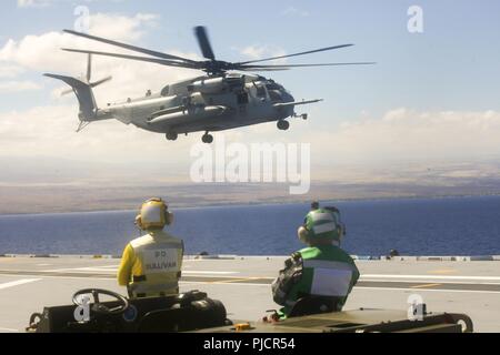 HMAS ADELAIDE der Royal Australian Navy flightline Besatzungsmitglieder Watch als US Marine Corps CH-53E Super Stallion Hubschrauber aus Aufzügen in touch down Operationen an Bord der Royal Australian Navy landing Helicopter dock Schiff HMAS Adelaide (L01) als Teil der Felge im Pazifik (Rimpac) Übung vor der Küste von Hawaii, 22. Juli 2018. RIMPAC bietet hochwertige Ausbildung für Task-organisierte, hoch-fähigen Marine-Air Boden Task Force und erhöht die kritische Reaktion auf Krisen Fähigkeit der US-Marines im Pazifik. 25 Nationen, mehr als 45 Schiffe und u-Boote, über 200 Flugzeuge und 25,00 Stockfoto