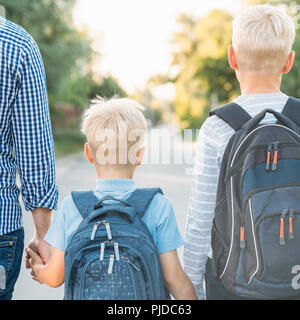 Vater und zwei Söhne, Hände halten und in die Schule zu gehen. Jungen mit Schultasche. Zurück zum Konzept der Schule. Stockfoto