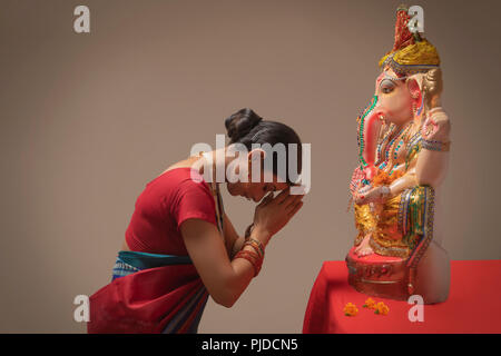 Betende Frau mit Händen und Augen vor ganpati Idol geschlossen. Stockfoto