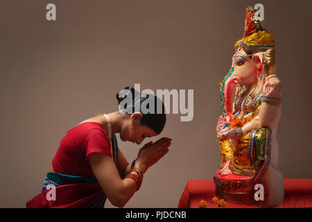 Betende Frau mit Händen und Augen vor ganpati Idol geschlossen. Stockfoto