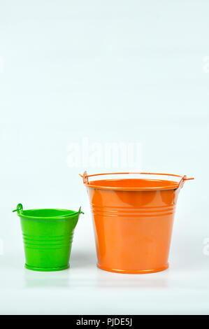 Kleine orange und grüne Eimer auf weißem Hintergrund. Stockfoto