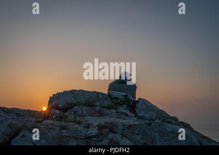 St. Ives, England - Mai 2018: Mann sitzt auf einem Felsen und bewundern Sie den Sonnenuntergang über der Cornwall, Cornwall Stockfoto